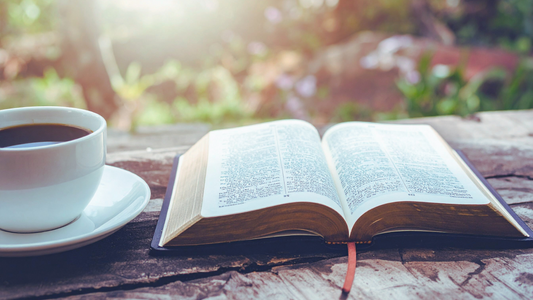 Picture of an open bible in the morning sunrise next to a cup of Christina's Coffee  Bayou Blend Medium Roast Coffee